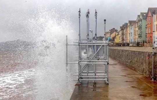 Photo of waves crashing onto a scaffolding structure on a promenade.