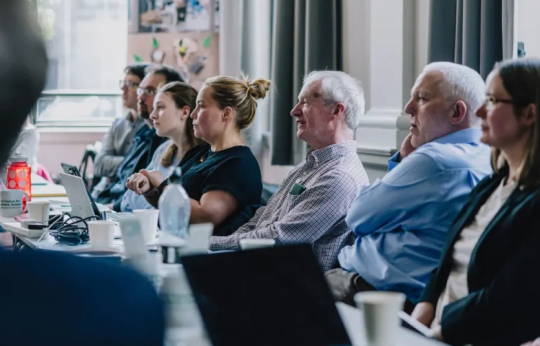 Seven people sat along a table all looking the same direction.