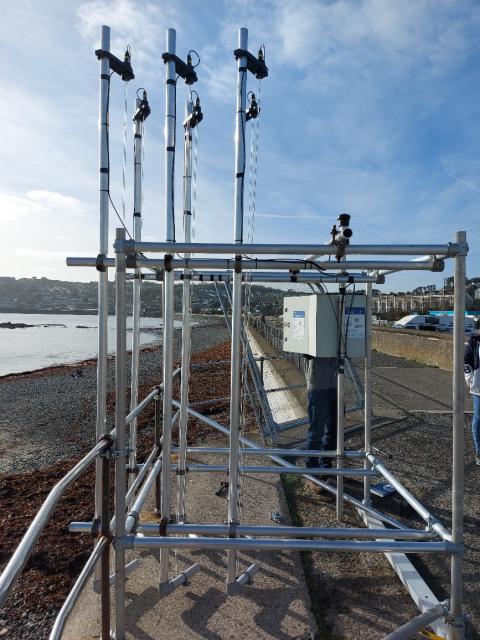 A photo of a scaffold of poles supporting sensors, positioned on the coast